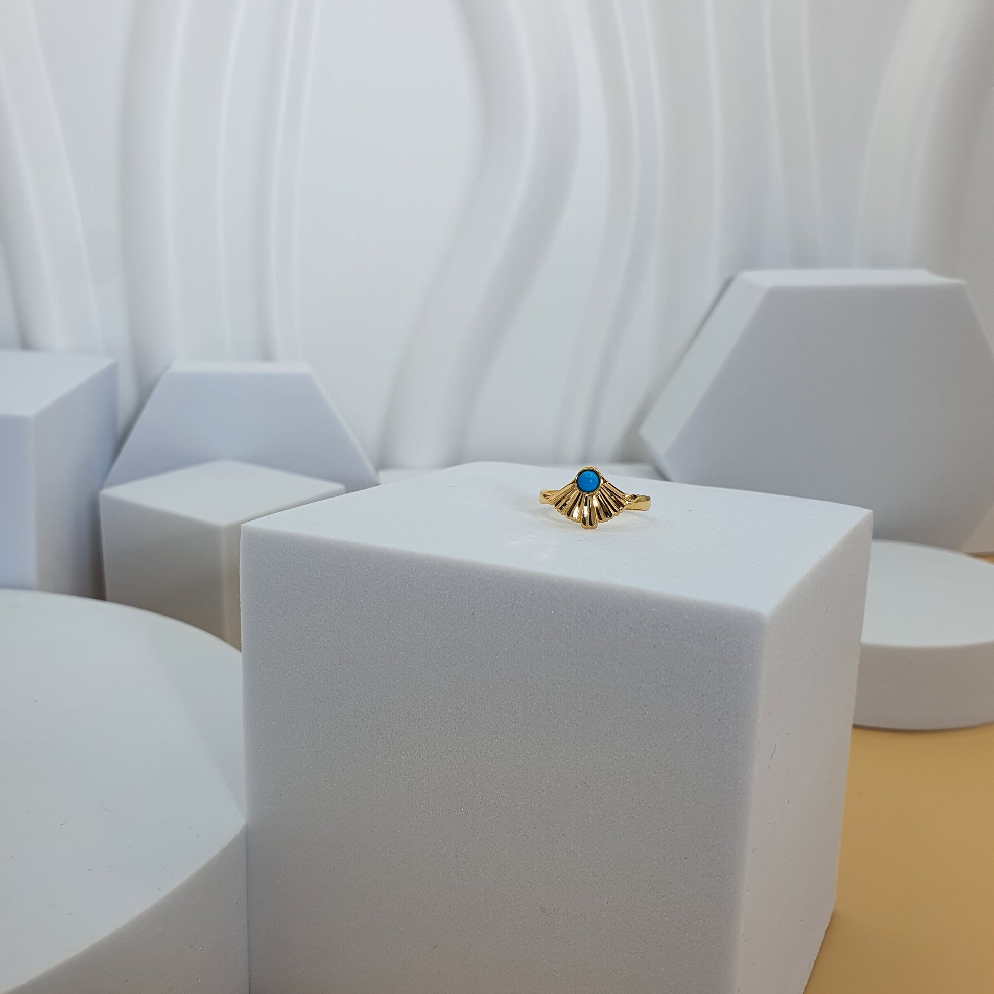 Gold earring with a blue gemstone on a white stand